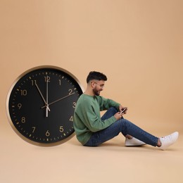 Man with smartphone and big clock on beige background