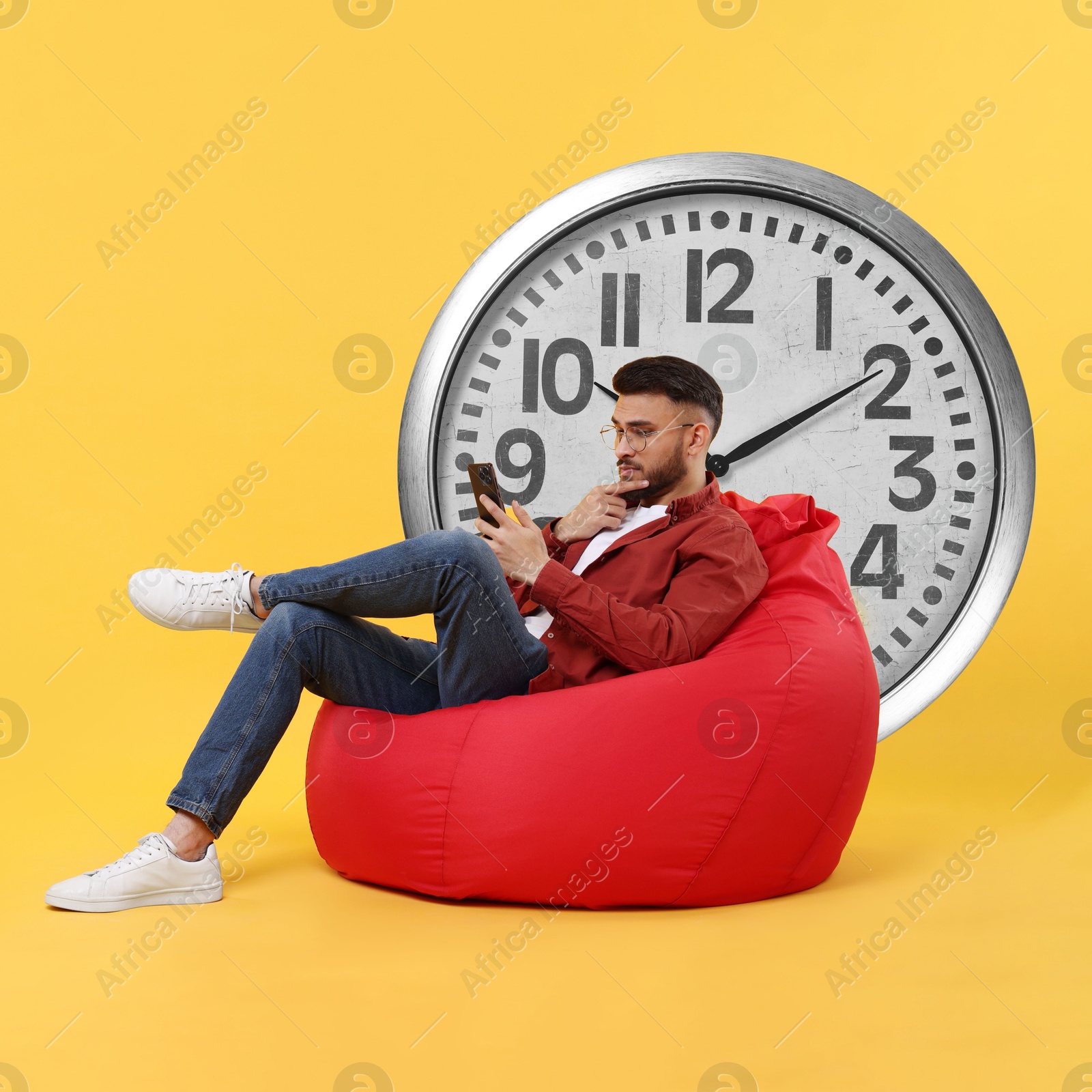 Image of Man with smartphone sitting in beanbag near big clock on orange background