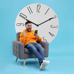 Happy man with smartphone sitting in armchair near big clock on light blue background