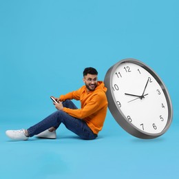 Man with smartphone and big clock on light blue background