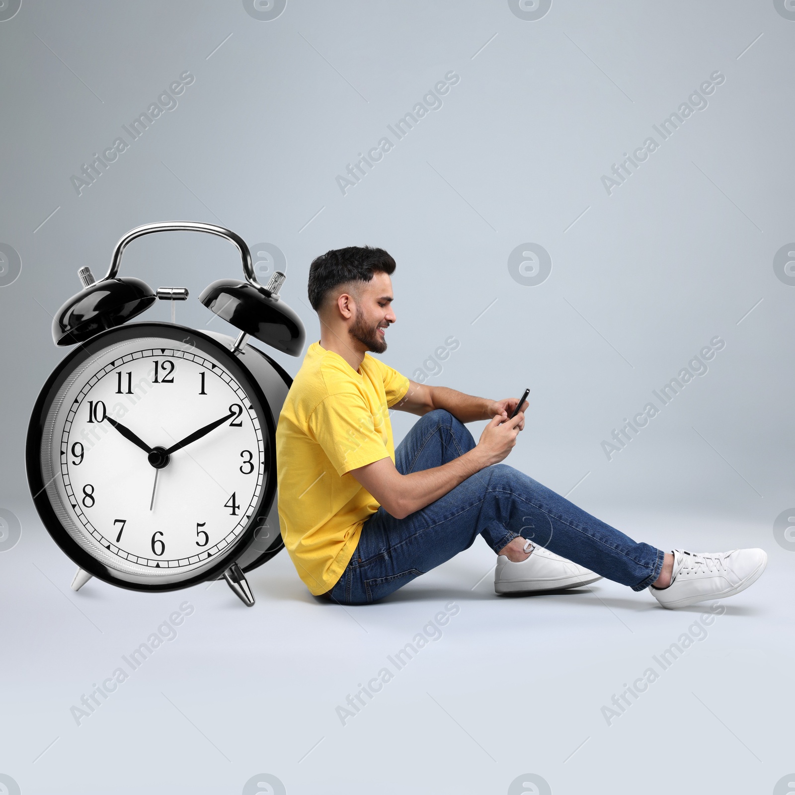 Image of Man with smartphone and big alarm clock on grey background