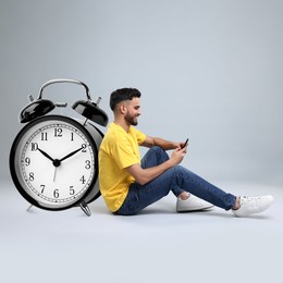 Image of Man with smartphone and big alarm clock on grey background