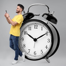 Man with smartphone and big alarm clock on grey background