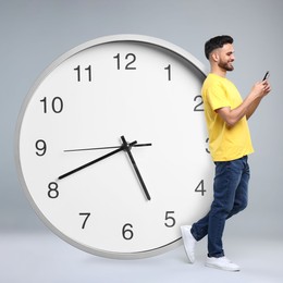 Man with smartphone and big clock on grey background