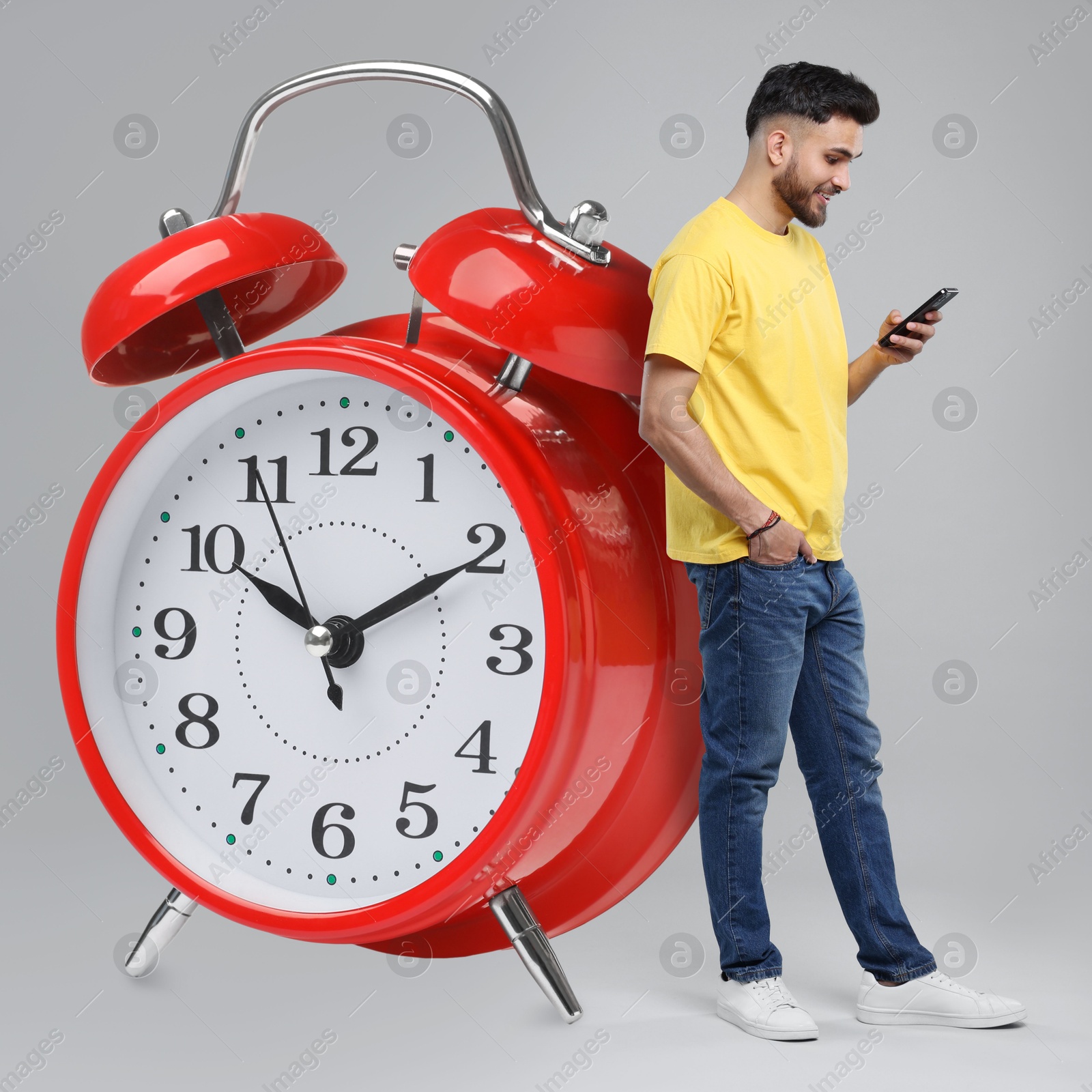 Image of Man with smartphone and big alarm clock on grey background