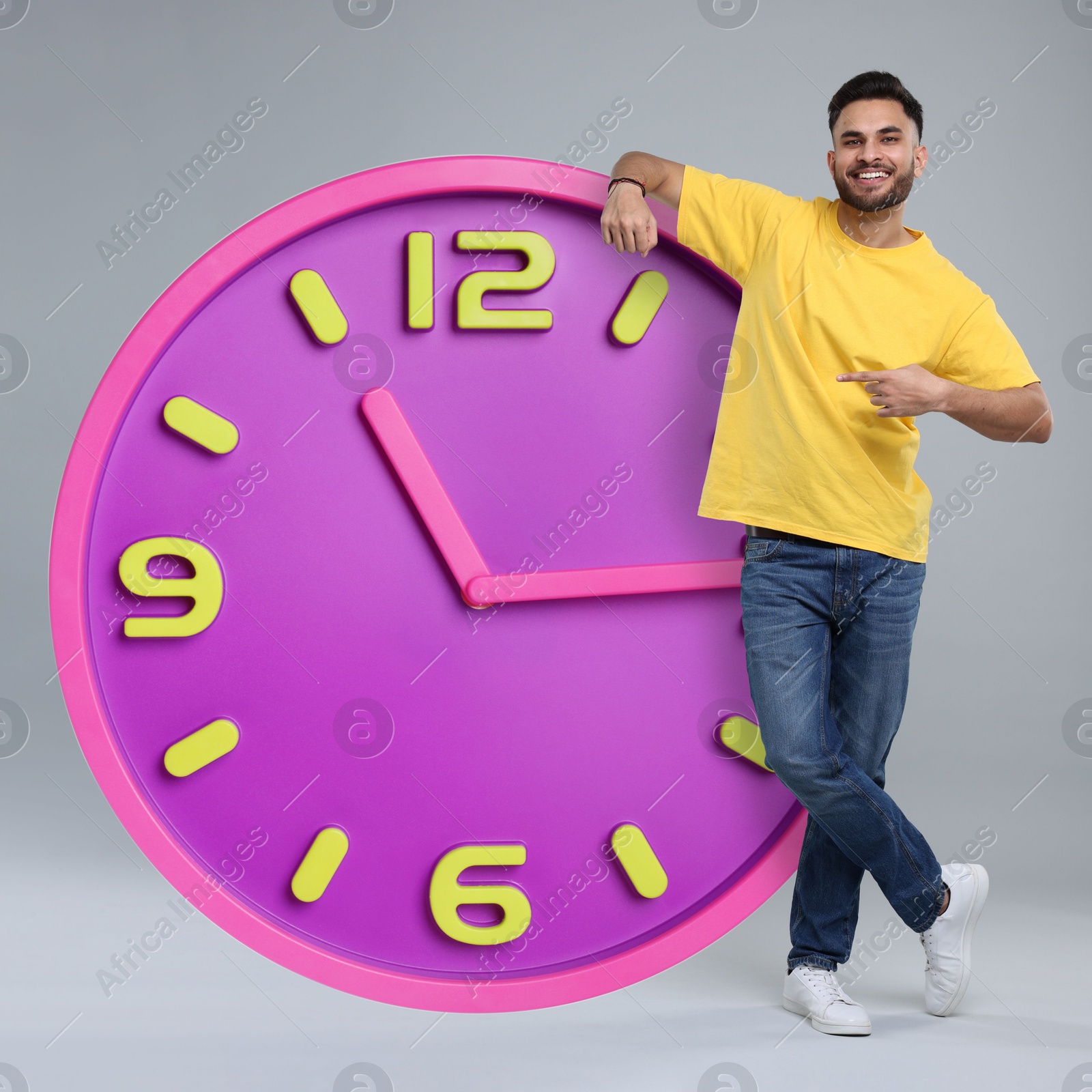 Image of Man pointing at big clock on grey background