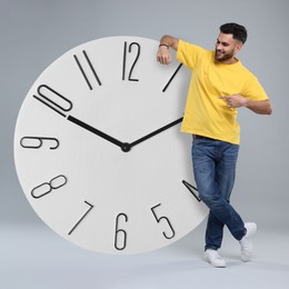 Man pointing at big clock on grey background