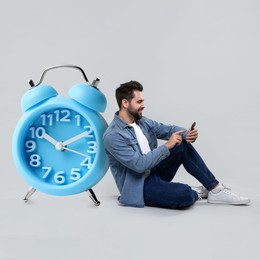 Man with smartphone and big alarm clock on grey background