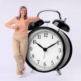 Image of Mature woman pointing at big alarm clock on white background