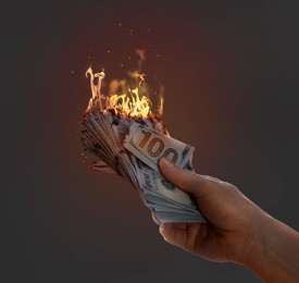 Image of Woman holding burning money on dark grey background, closeup. Financial crisis