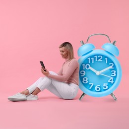 Image of Woman with smartphone and big alarm clock on pink background