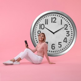 Image of Woman with smartphone and big clock on pink background