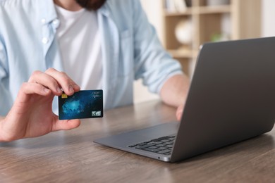 Photo of Online banking. Young man with credit card and laptop paying purchase at table indoors, closeup