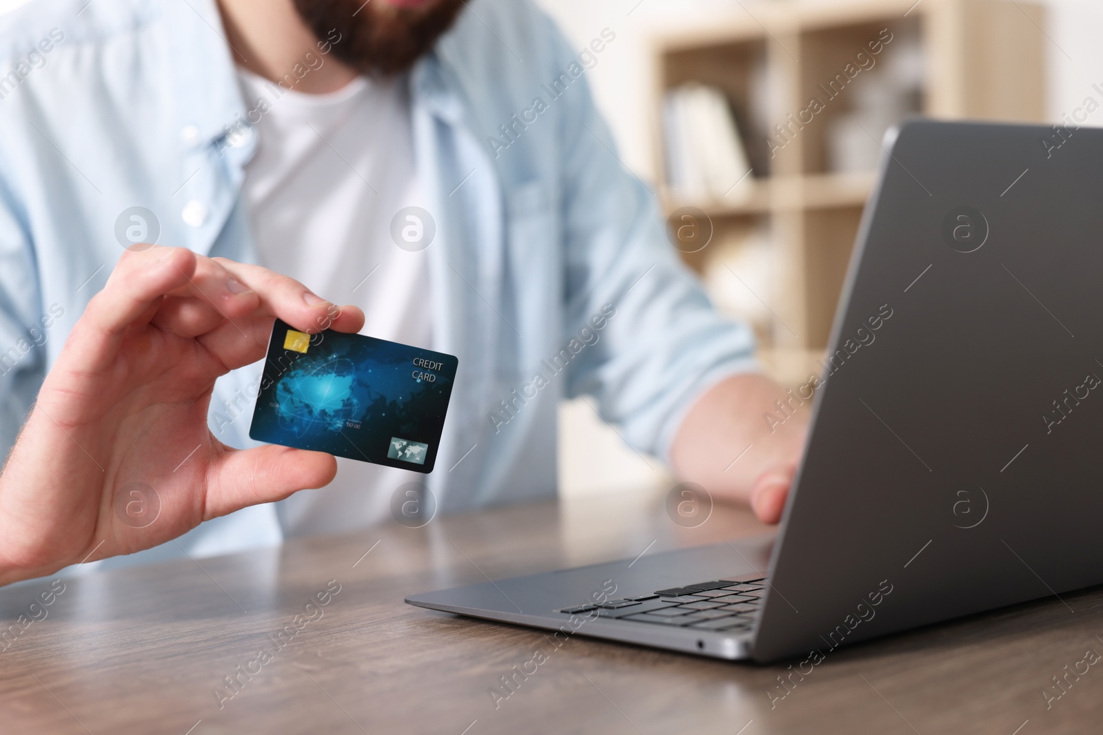 Photo of Online banking. Young man with credit card and laptop paying purchase at table indoors, closeup