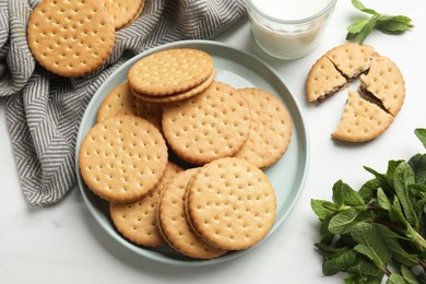 Tasty sandwich cookies, glass of milk and mint on white table, above view