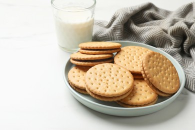 Tasty sandwich cookies and glass of milk on white table, closeup. Space for text