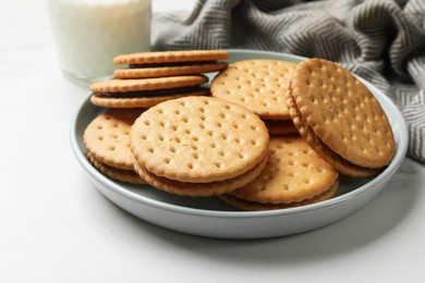 Photo of Tasty sandwich cookies and glass of milk on white table, closeup