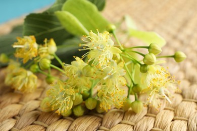 Fresh linden leaves and flowers on wicker mat, closeup