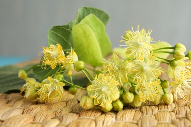 Photo of Fresh linden leaves and flowers on wicker mat, closeup