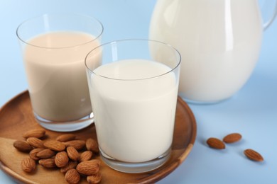 Photo of Fresh almond milk in glasses and nuts on light blue background