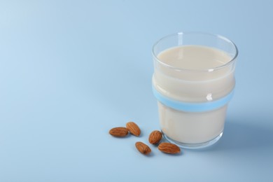 Fresh almond milk in glass and nuts on light blue background, space for text