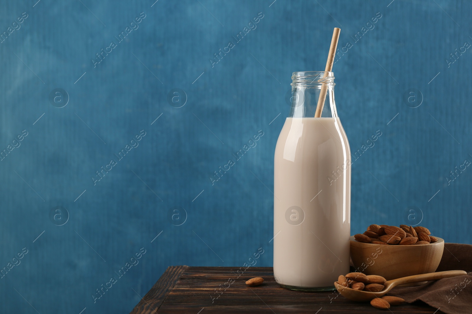 Photo of Fresh almond milk in glass bottle, nuts and spoon on wooden table, space for text