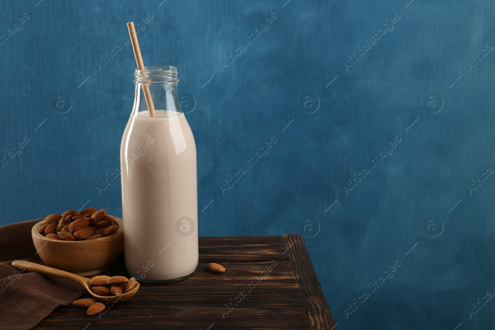 Photo of Fresh almond milk in glass bottle, nuts and spoon on wooden table, space for text