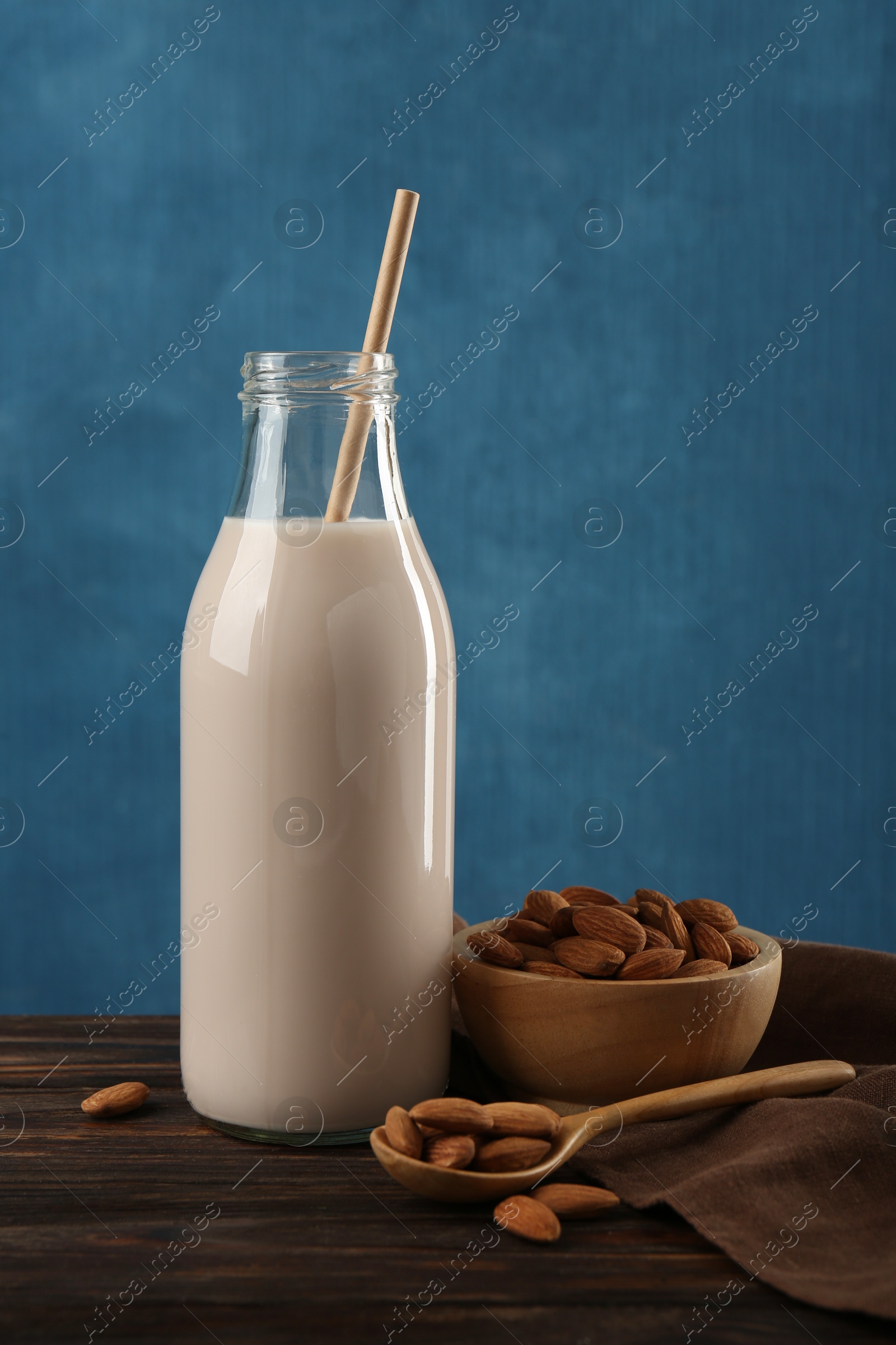 Photo of Fresh almond milk in glass bottle, nuts and spoon on wooden table