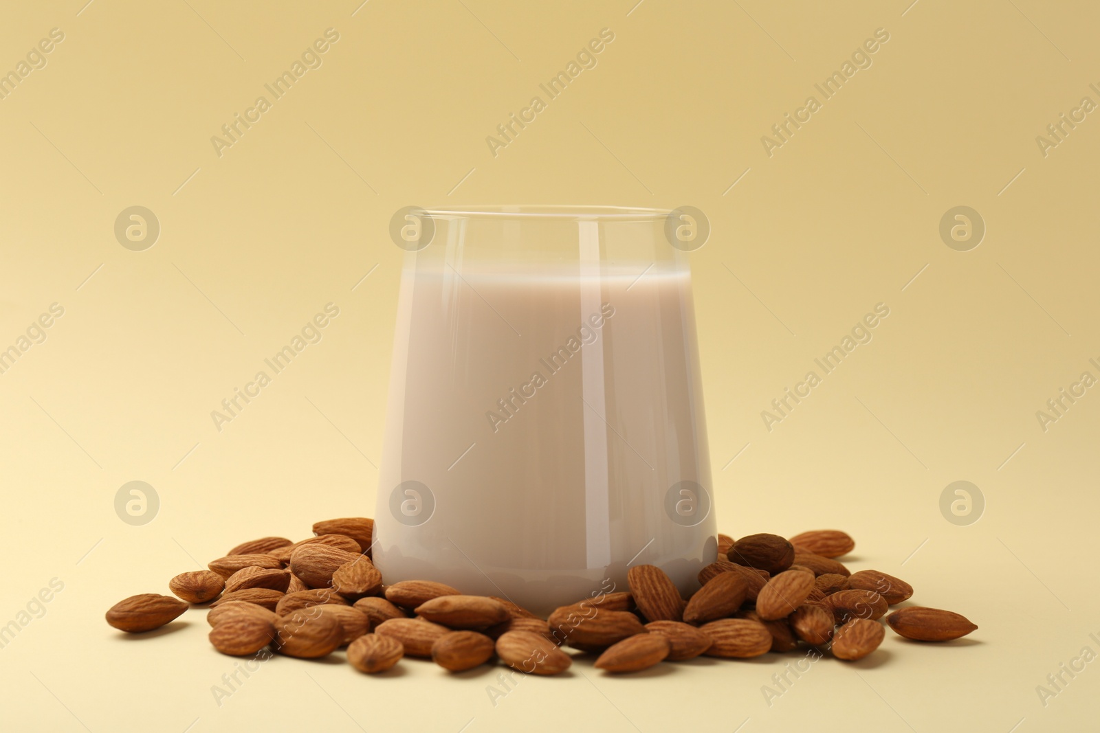 Photo of Fresh almond milk in glass and nuts on beige background