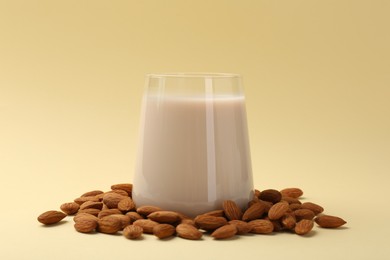 Photo of Fresh almond milk in glass and nuts on beige background