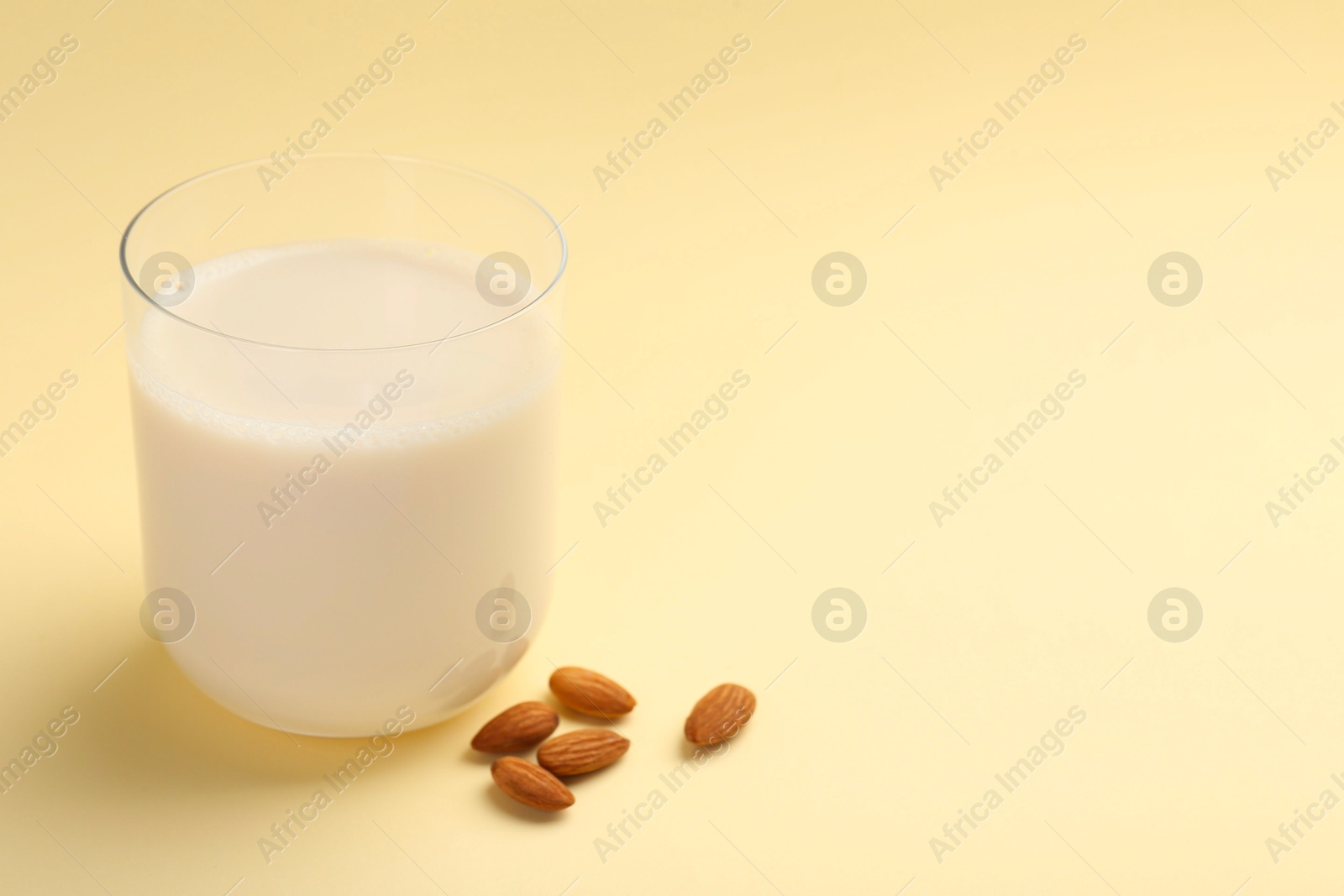 Photo of Fresh almond milk in glass and nuts on beige background, space for text