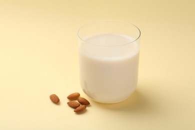 Photo of Fresh almond milk in glass and nuts on beige background