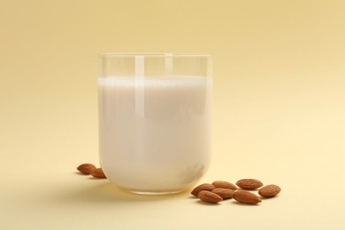 Fresh almond milk in glass and nuts on beige background