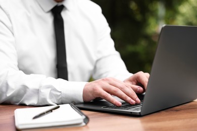 Photo of Businessman working with laptop at table outdoors, closeup. Remote job