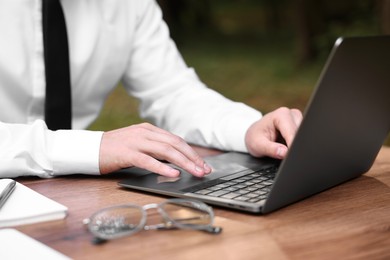 Photo of Businessman working with laptop at table outdoors, closeup. Remote job