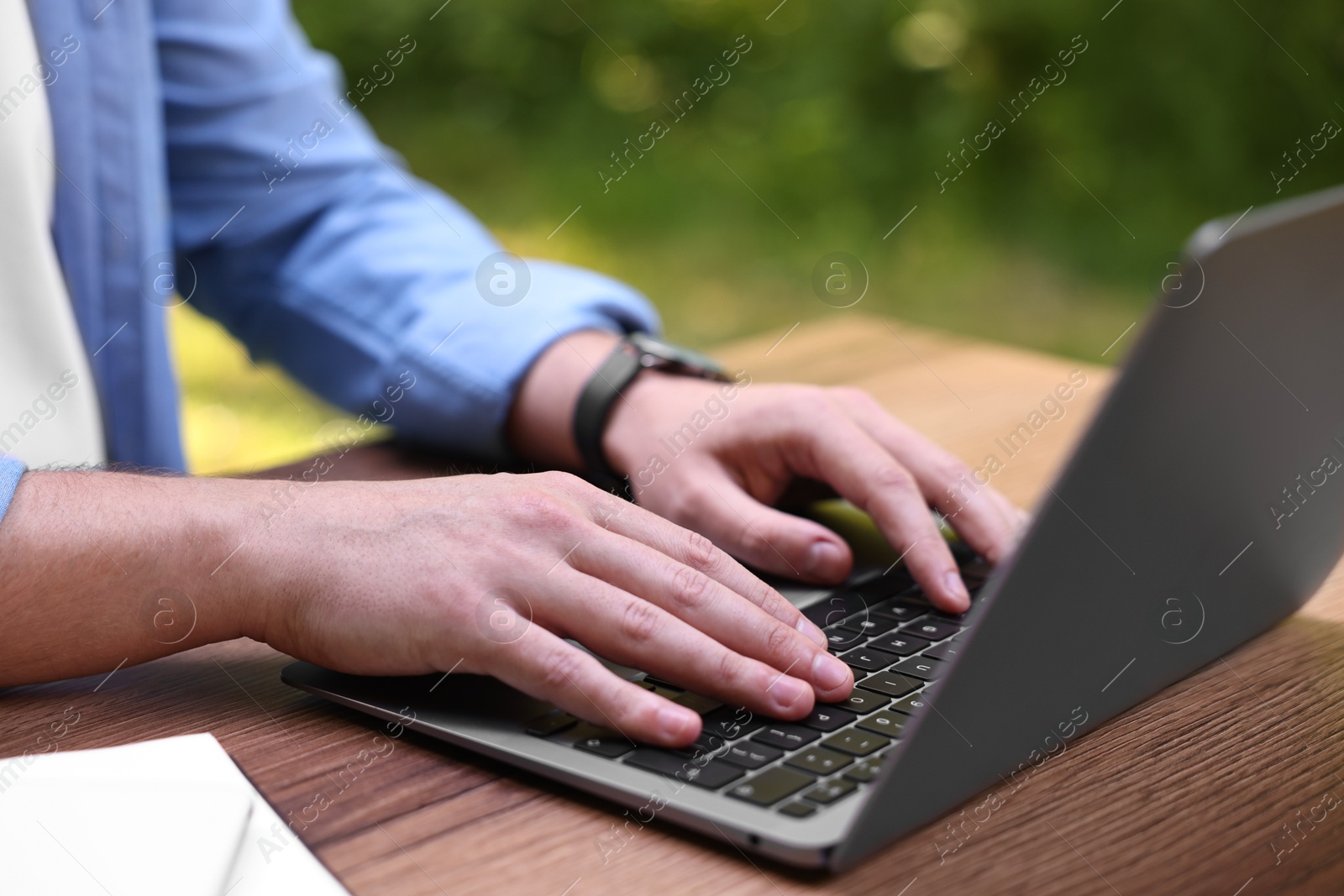 Photo of Freelancer working with laptop at wooden table outdoors, closeup. Remote job