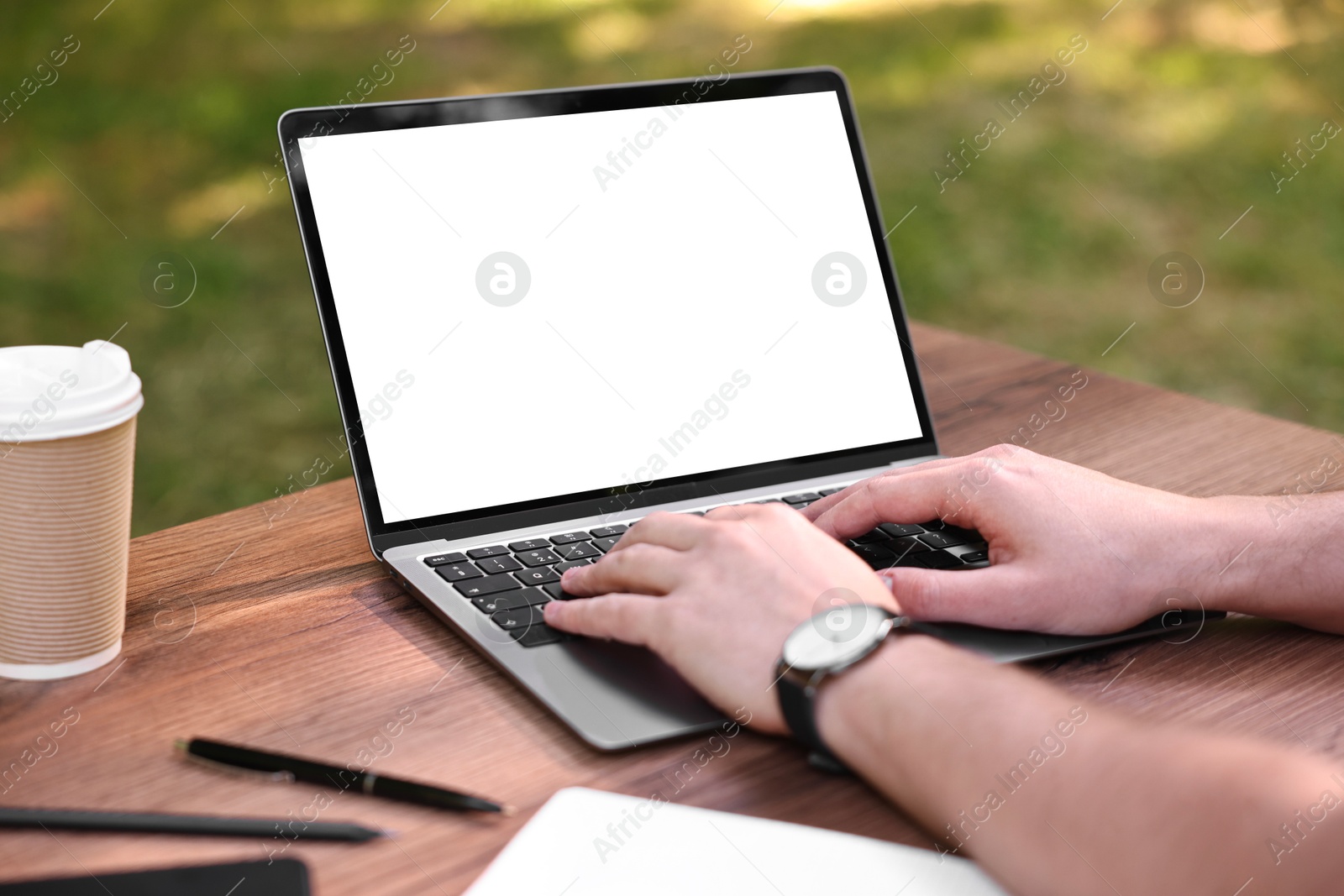 Photo of Freelancer working with laptop at wooden table outdoors, closeup. Remote job