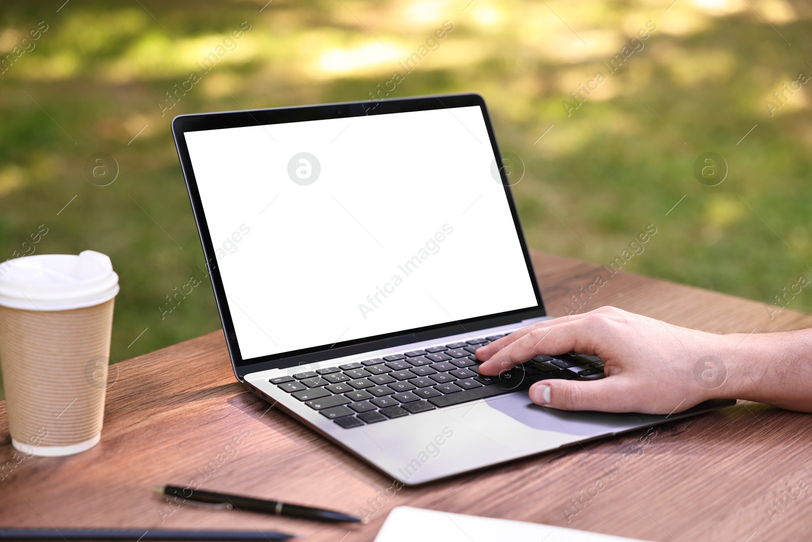 Photo of Freelancer working with laptop at wooden table outdoors, closeup. Remote job