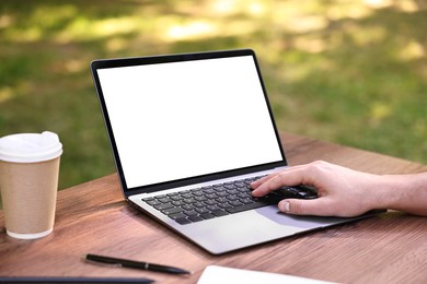 Photo of Freelancer working with laptop at wooden table outdoors, closeup. Remote job