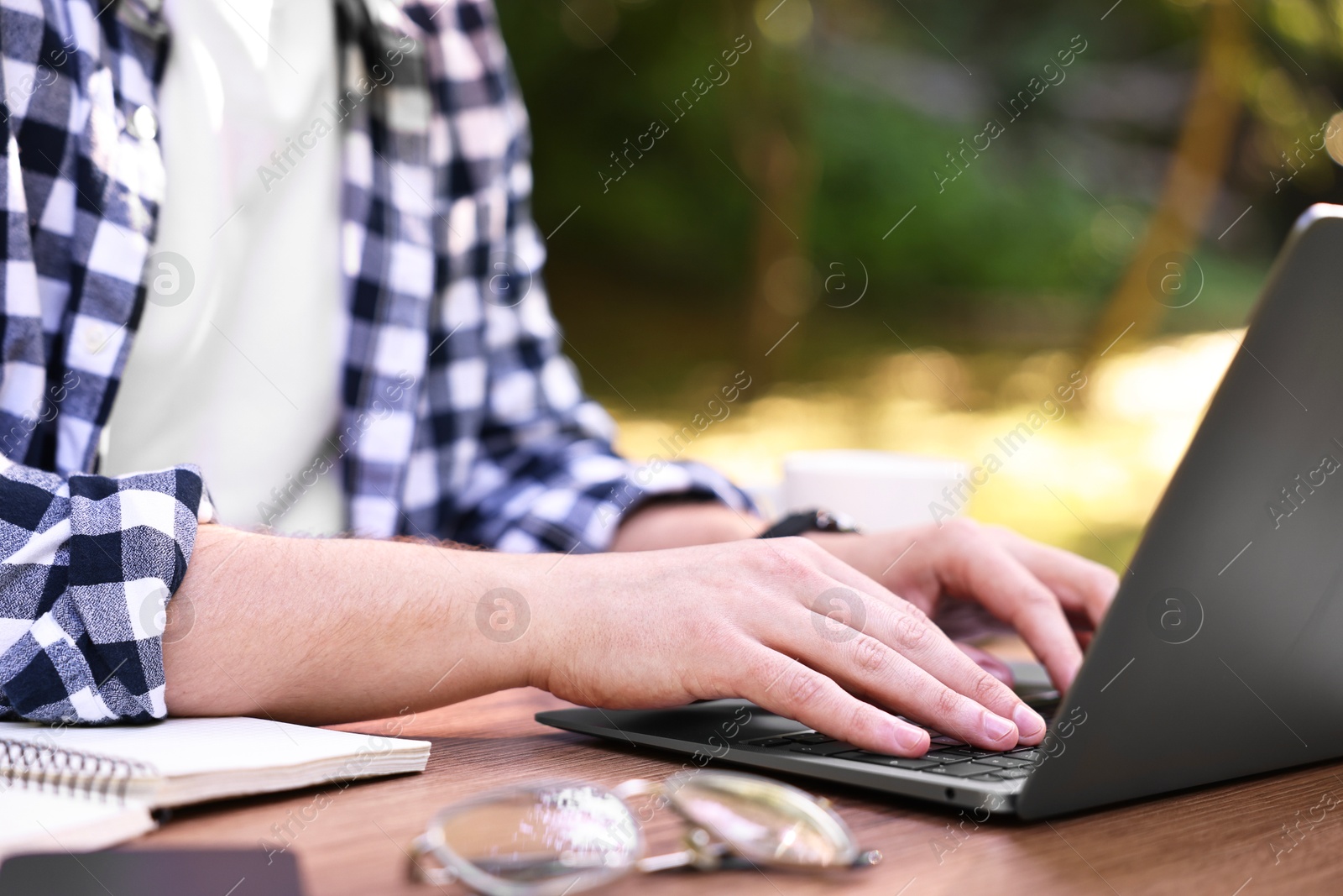 Photo of Freelancer working with laptop at wooden table outdoors, closeup. Remote job