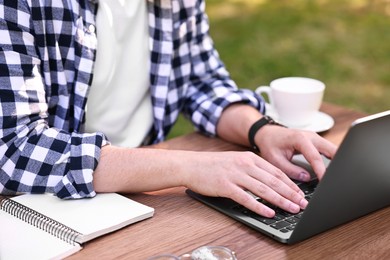 Photo of Freelancer working with laptop at wooden table outdoors, closeup. Remote job