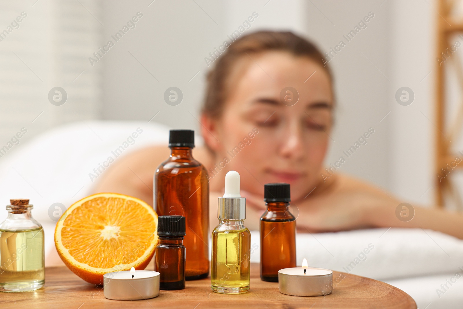 Photo of Aromatherapy. Woman relaxing on massage couch in spa salon, focus on bottles of essential oils, orange and burning candles