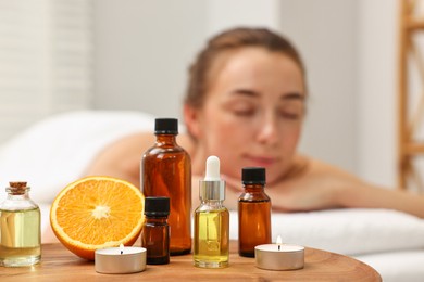 Photo of Aromatherapy. Woman relaxing on massage couch in spa salon, focus on bottles of essential oils, orange and burning candles