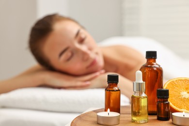 Aromatherapy. Woman relaxing on massage couch in spa salon, focus on bottles of essential oils, orange and burning candles