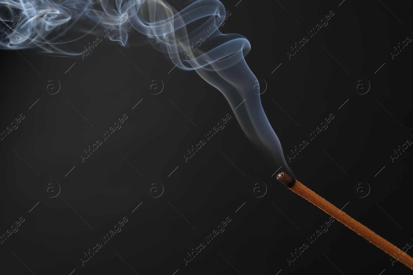 Photo of Aromatic incense stick smoldering on black background, closeup