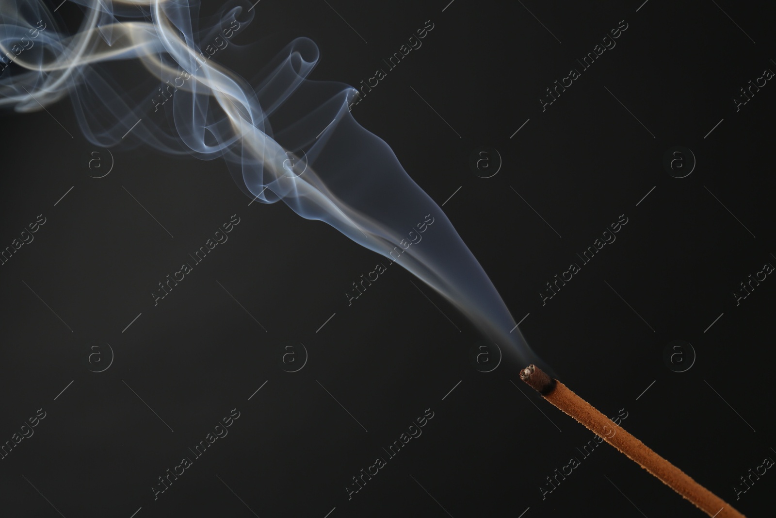 Photo of Aromatic incense stick smoldering on black background, closeup