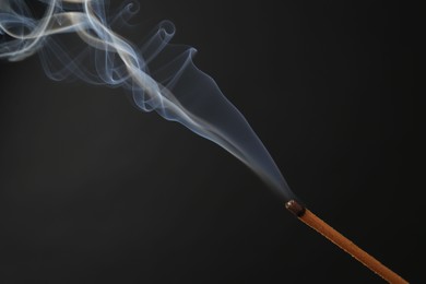 Photo of Aromatic incense stick smoldering on black background, closeup