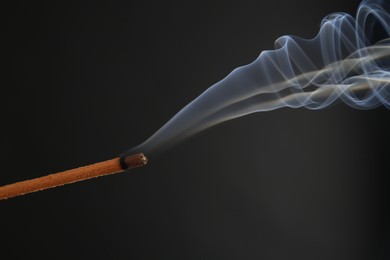 Aromatic incense stick smoldering on black background, closeup