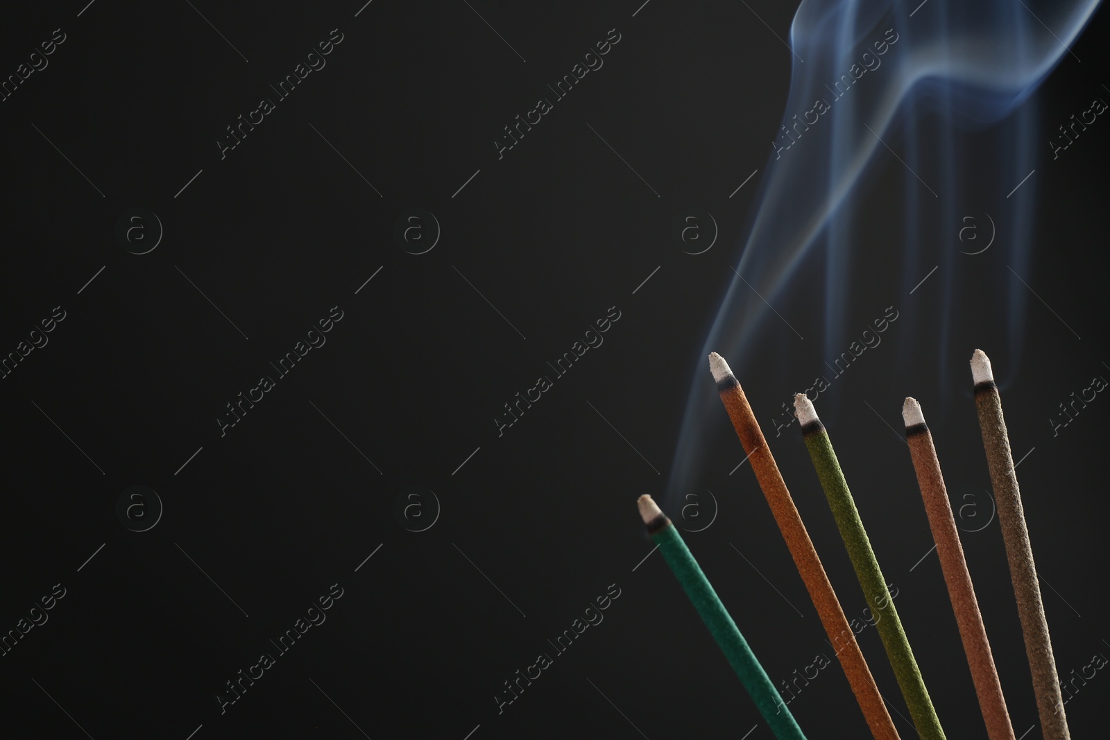 Photo of Aromatic incense sticks smoldering on black background. Space for text