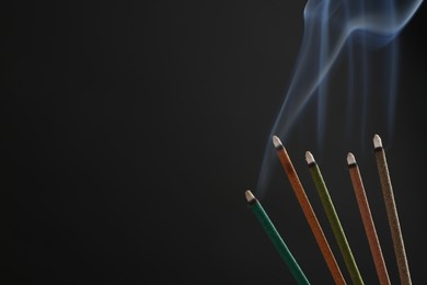 Photo of Aromatic incense sticks smoldering on black background. Space for text